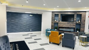 Un vestíbulo moderno con una gran pared azul oscuro, un televisor de pantalla plana y una chimenea. Hay varias zonas de estar con sofás y sillones.