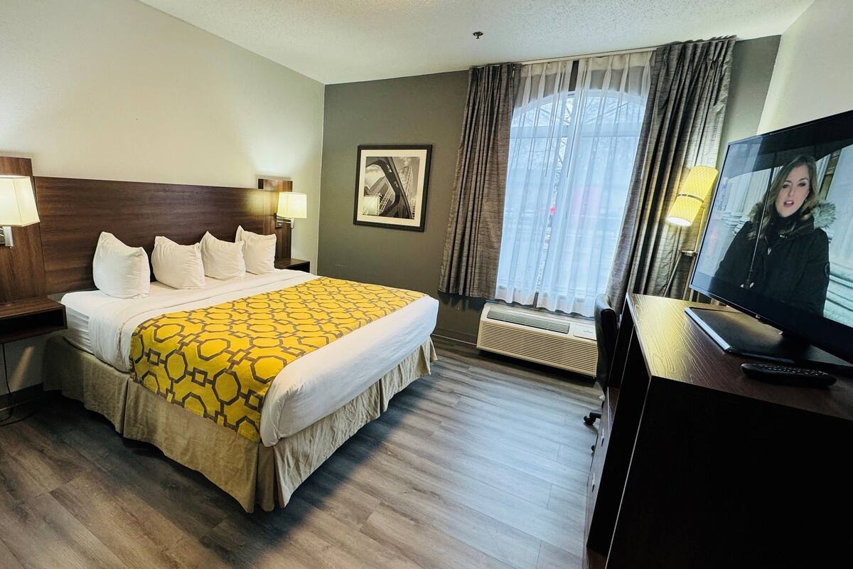 Een hotelkamer met een groot bed, twee bedlampen, een televisie en een raam met gordijnen.