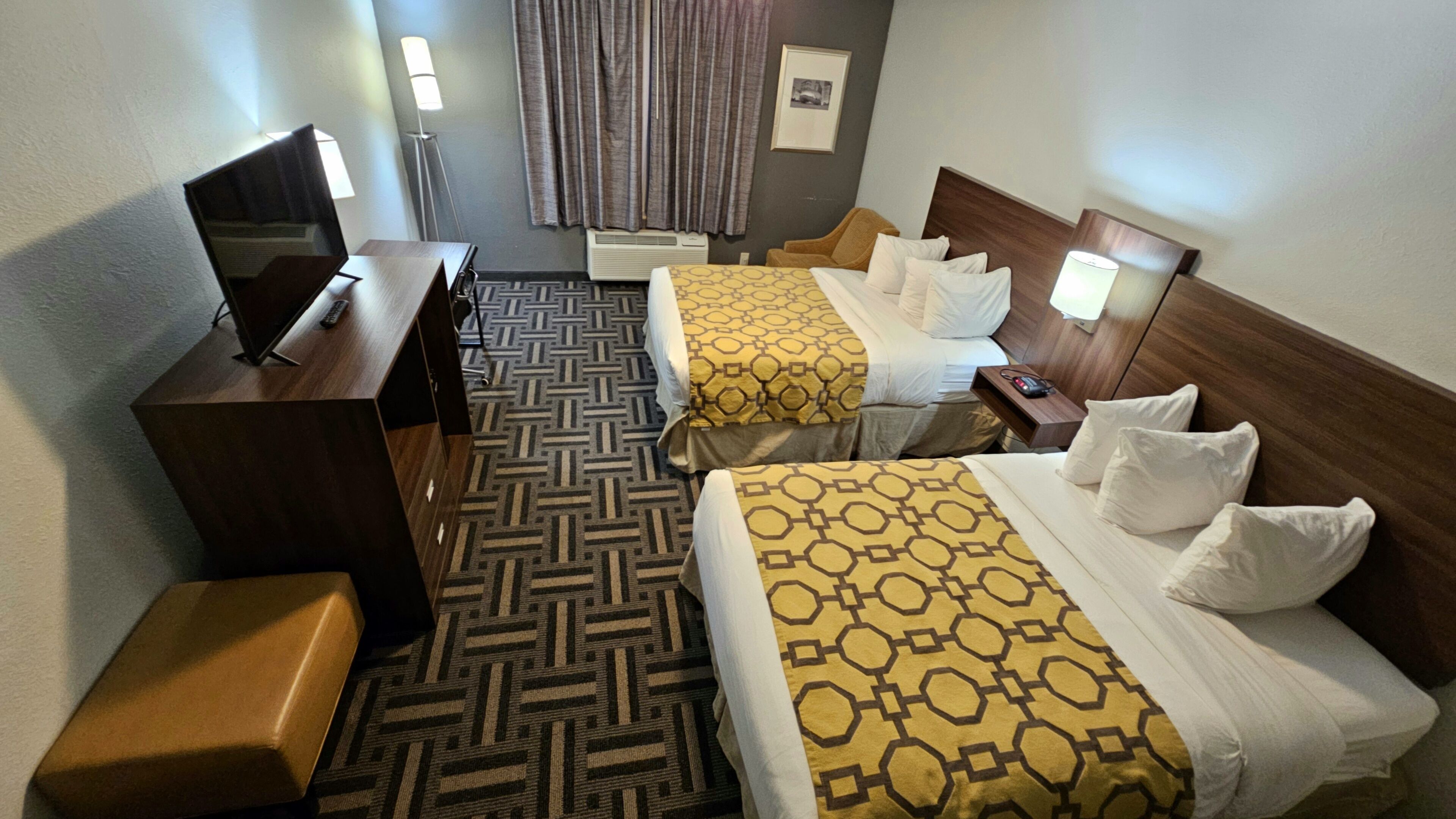 A hotel room with two beds, a desk, a chair, a TV, and a floor lamp.