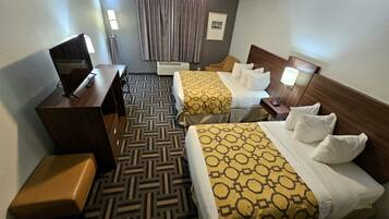 A hotel room with two beds, a desk, a chair, a TV, and a floor lamp.