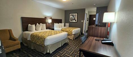 A hotel room with two beds, a desk, a chair, a desk lamp, a phone, and a TV.