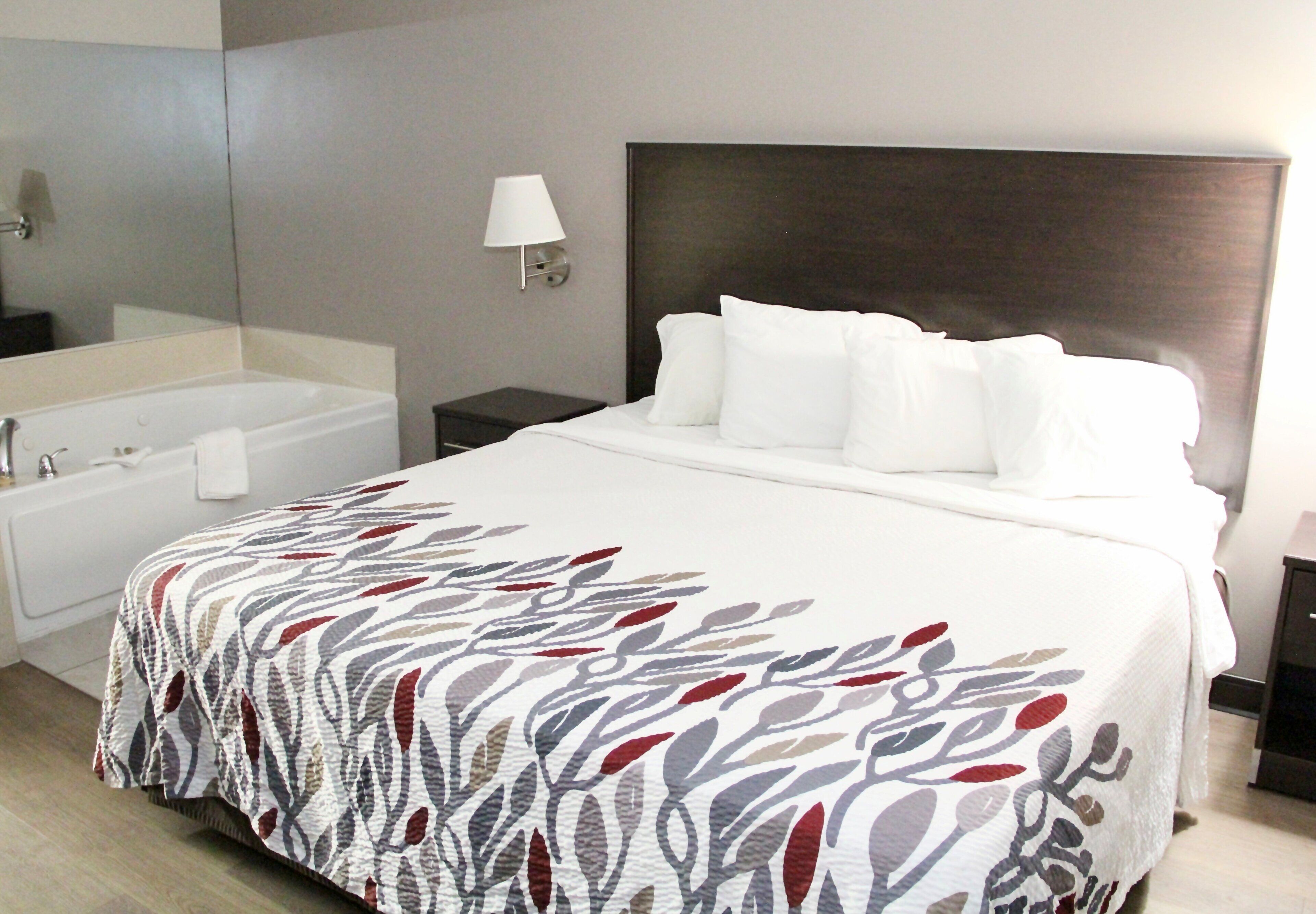A hotel room with a large bed, a separate bathroom with a bathtub, and a nightstand with a lamp.