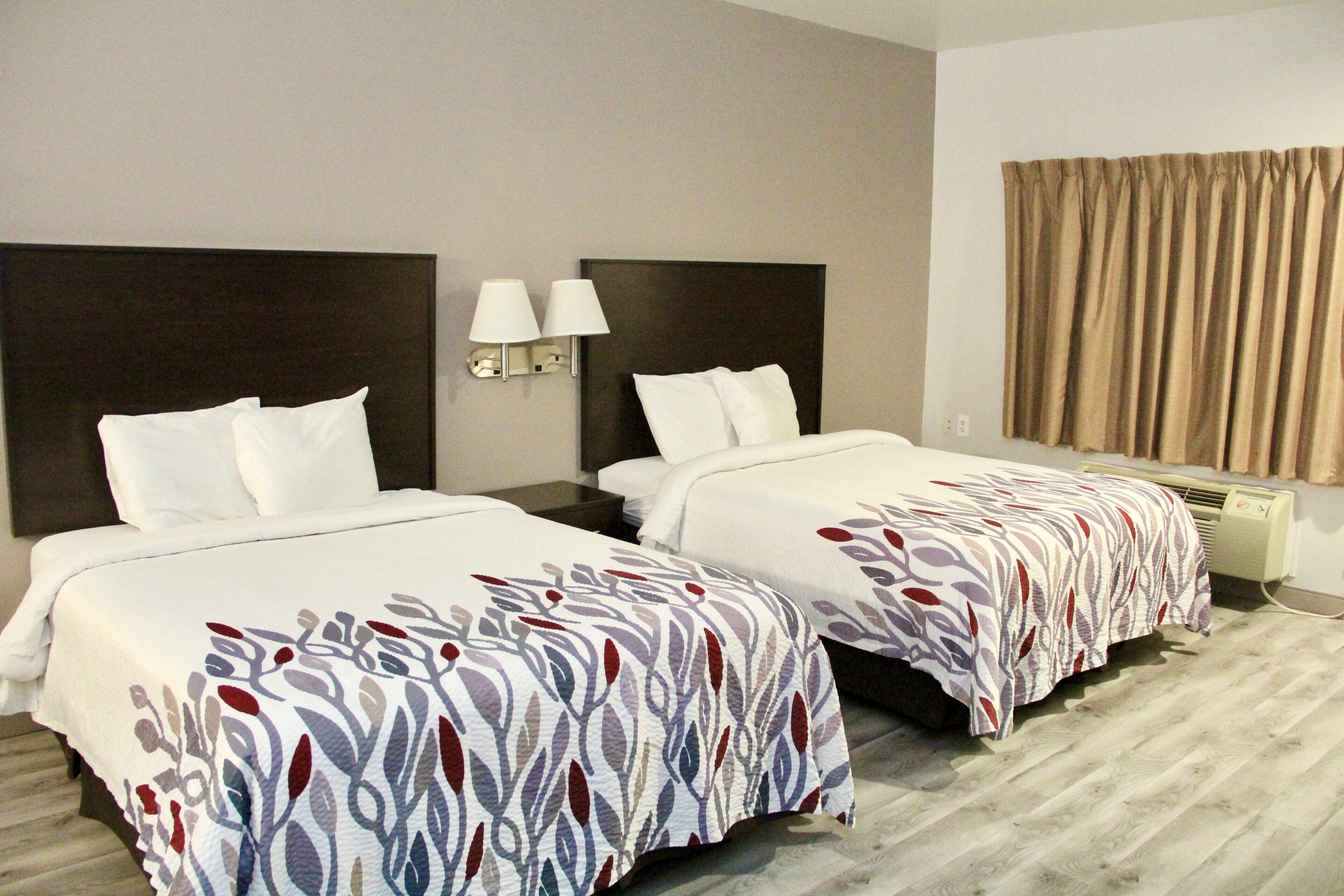 Habitación de hotel con dos camas, cada una con cabecera, mesita de noche, lámpara y ventana con cortinas.