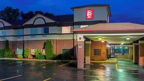 Hotel com entrada coberta, estacionamento e fachada de tijolos.