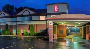 A hotel with a covered entrance, a parking lot, and a brick facade.