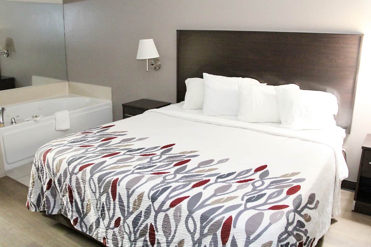 A hotel room with a large bed, a separate bathroom with a bathtub, and a nightstand with a lamp.