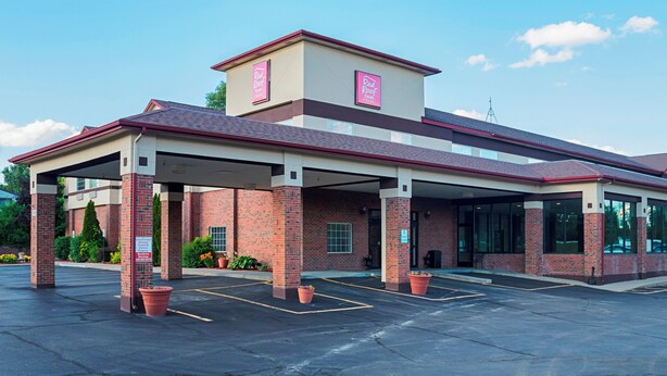 Um Red Roof Inn com fachada de tijolos, estacionamento coberto e céu limpo.