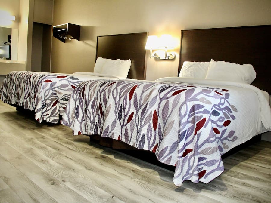 Una camera d'albergo con due letti, ciascuno con una coperta a motivi, un comodino, una lampada a parete e un pavimento in legno.