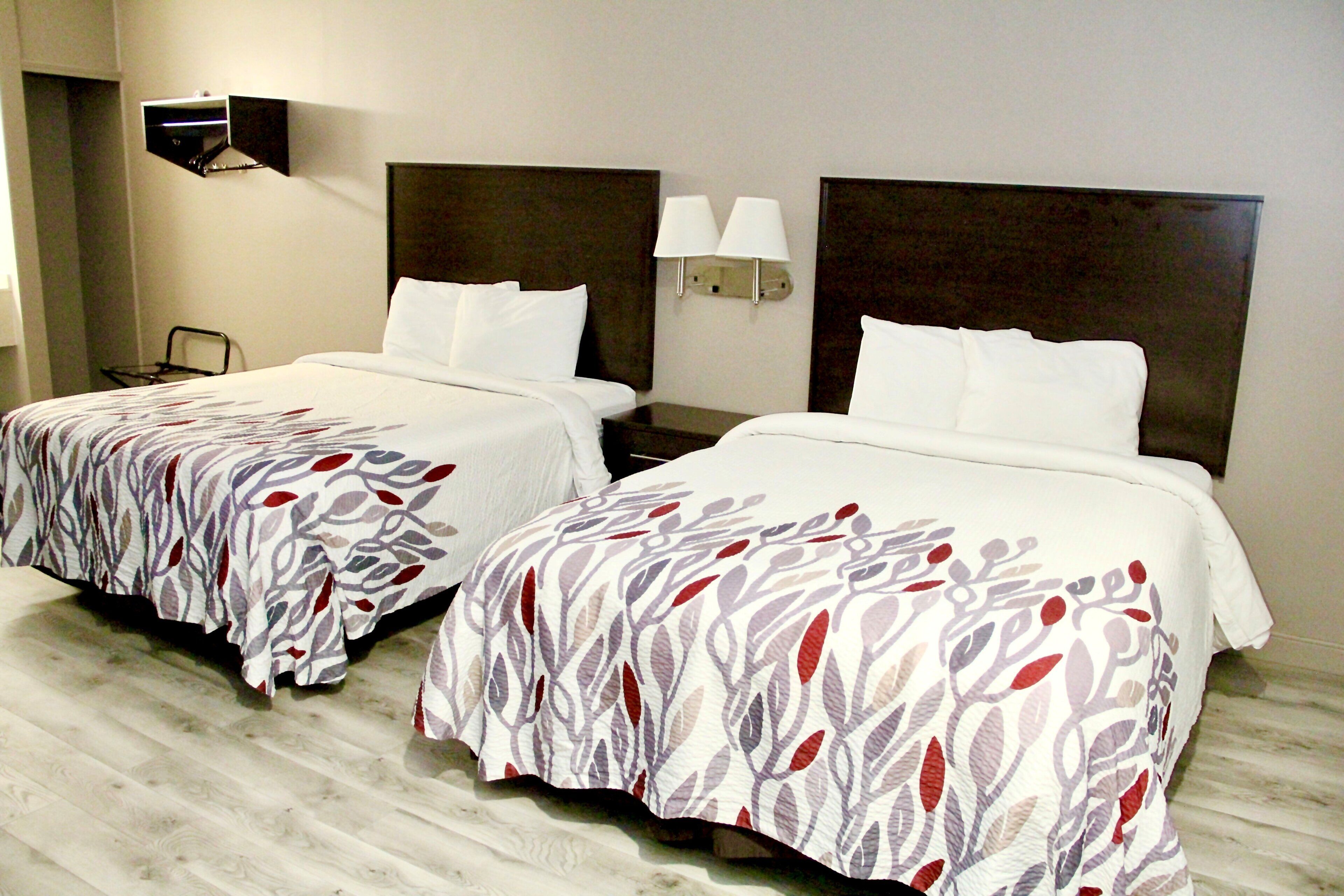 Ein Hotelzimmer mit zwei Betten, jeweils mit Kopfteil und Nachttischen. An jeder Seite der Betten befinden sich Wandlampen.
