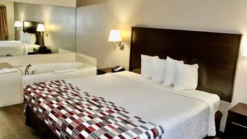 A hotel room with a large bed, a separate bathroom with a bathtub, a nightstand with a lamp, and a mirror above the bed.