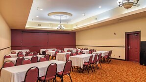 Une salle de conférence avec plusieurs tables et chaises, une moquette à motifs et une porte rouge.