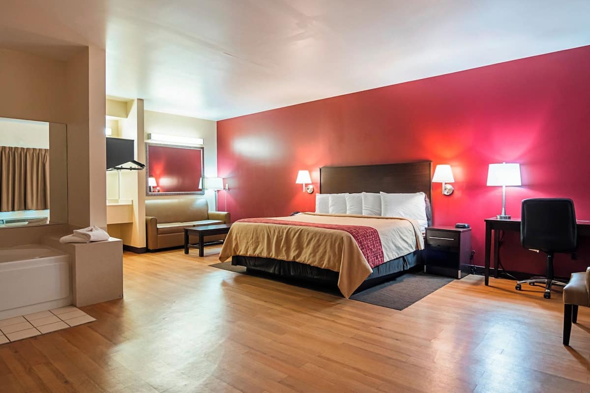 A hotel room with a bed, bedside tables, a desk, a chair, a sofa, and a mirror.