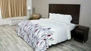 Une chambre d’hôtel avec un grand lit, une table de chevet, une chaise, une lampe et une fenêtre avec des rideaux.