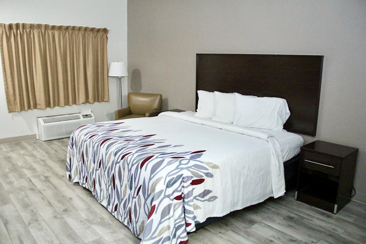A hotel room with a large bed, a bedside table, a chair, a lamp, and a window with curtains.