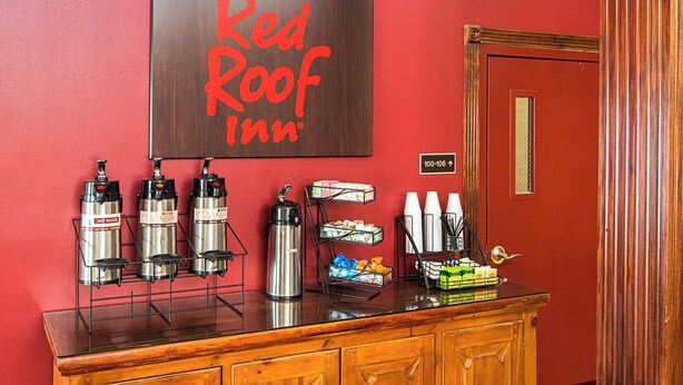 L'aire d'accueil d'un hôtel Red Roof Inn, avec un panneau d'affichage, des distributeurs d'eau chaude, un coin café et une porte portant une indication du numéro de chambre.