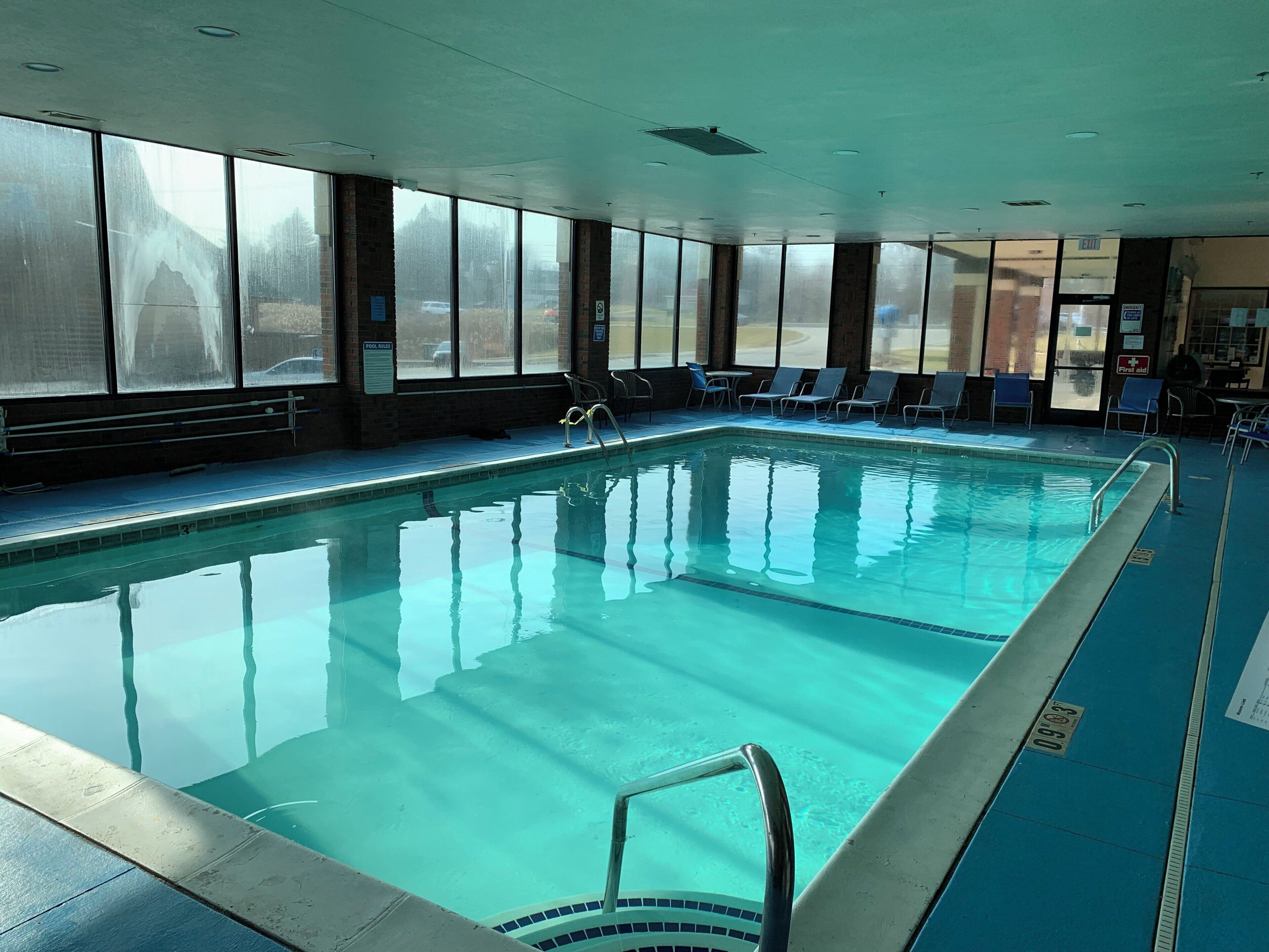 Una piscina interior con agua cristalina, rodeada de ventanas y sillones de descanso.