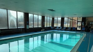Piscina interior com água cristalina, rodeada por janelas e espreguiçadeiras.