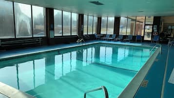 Una piscina interior con agua cristalina, rodeada de ventanas y sillones de descanso.