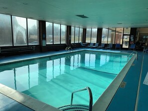 An indoor swimming pool with clear water, surrounded by windows and lounge chairs.