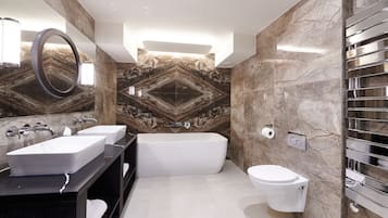 A modern bathroom with a freestanding bathtub, two sinks, and a toilet.