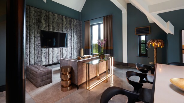 A modern living room with a marble-patterned wall, a flat-screen TV, a glass-top coffee table, and a seating area with a cushioned bench and chairs. - Aldwark Manor Estate (York)