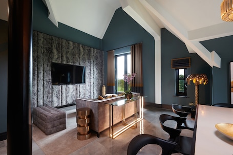 A modern living room with a marble-patterned wall, a flat-screen TV, a glass-top coffee table, and a seating area with a cushioned bench and chairs.