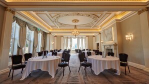 A formal dining room with round tables, chairs, chandeliers, and a fireplace. - Aldwark Manor Estate (York)