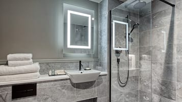 Un baño moderno con ducha envuelta en cristal, un lavamanos blanco e iluminación integrada en el espejo.