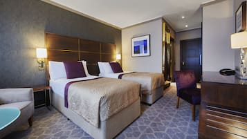 A hotel room with two beds, a desk, a chair, and a small table.