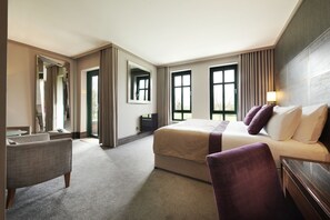A hotel room with a large bed, a seating area, and a view of the outdoors.