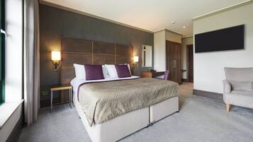 A modern hotel room with a large bed, bedside tables, a flat-screen TV, and a seating area with a sofa.