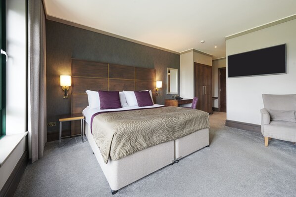 A modern hotel room with a large bed, bedside tables, a flat-screen TV, and a seating area with a sofa.