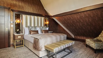 A bedroom with a large bed, a bench, a chair, and a nightstand with a lamp.