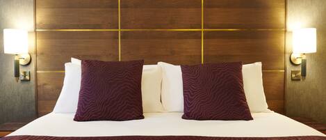 A hotel room with a large bed, two wall-mounted lamps, and a wooden headboard.