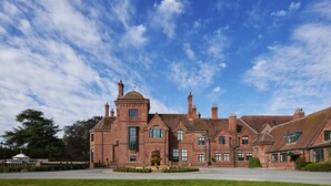 A large brick building with multiple chimneys, a central fountain, and a well-maintained lawn. - Aldwark Manor Estate (York)