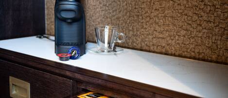 A coffee machine and a glass cup on a marble countertop.