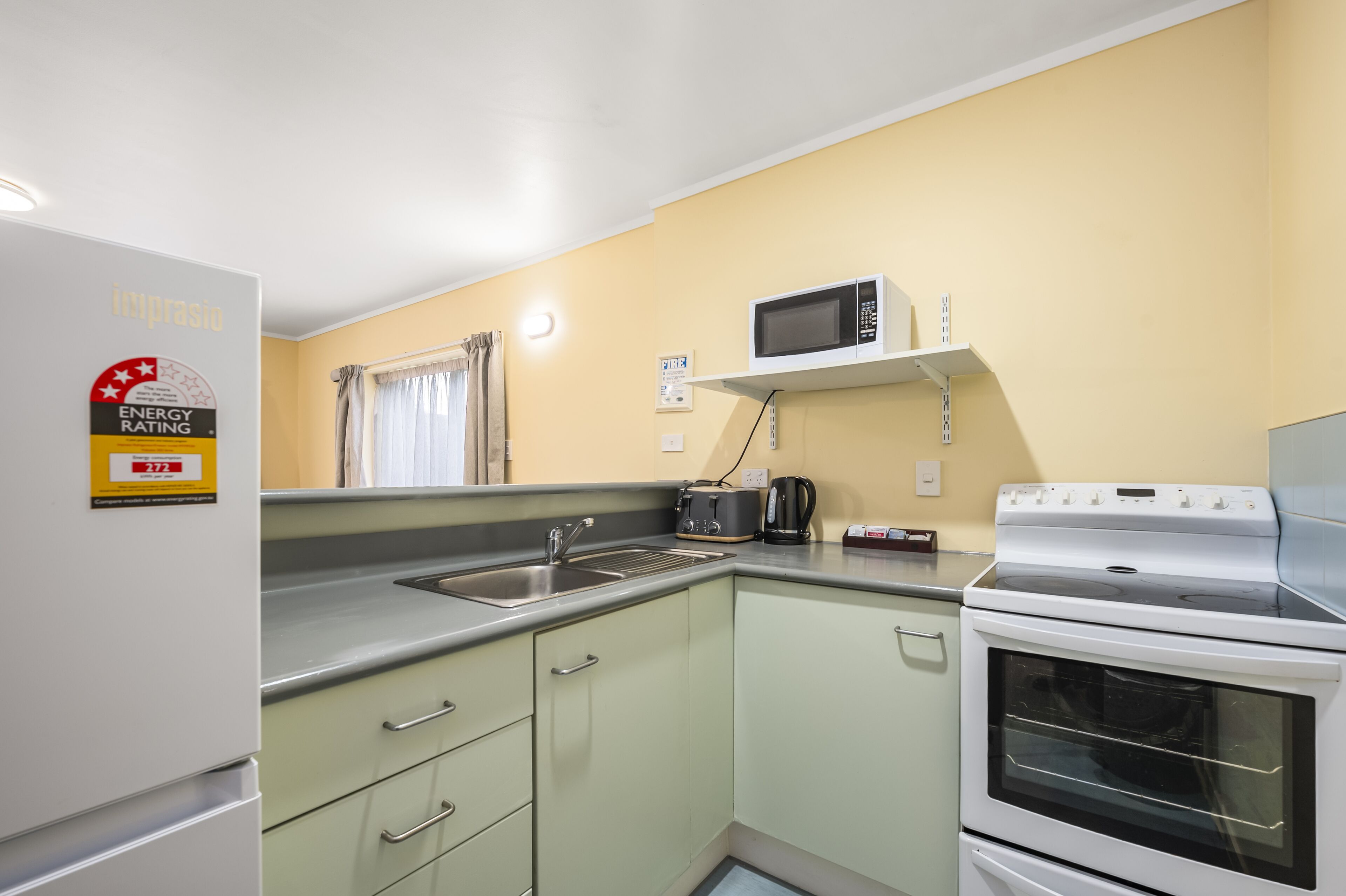 A compact kitchen with a white refrigerator, a microwave on a shelf, a stove, and a sink.