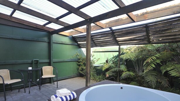 A covered outdoor area with a hot tub, two wicker chairs, and a small table. - Fenton Court Motel (Rotorua)
