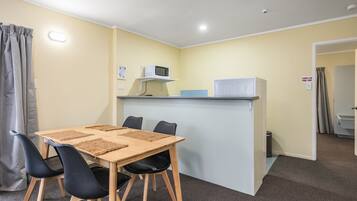 A small, compact room with a wooden table and four black chairs, a microwave, and a small refrigerator on a white shelf.