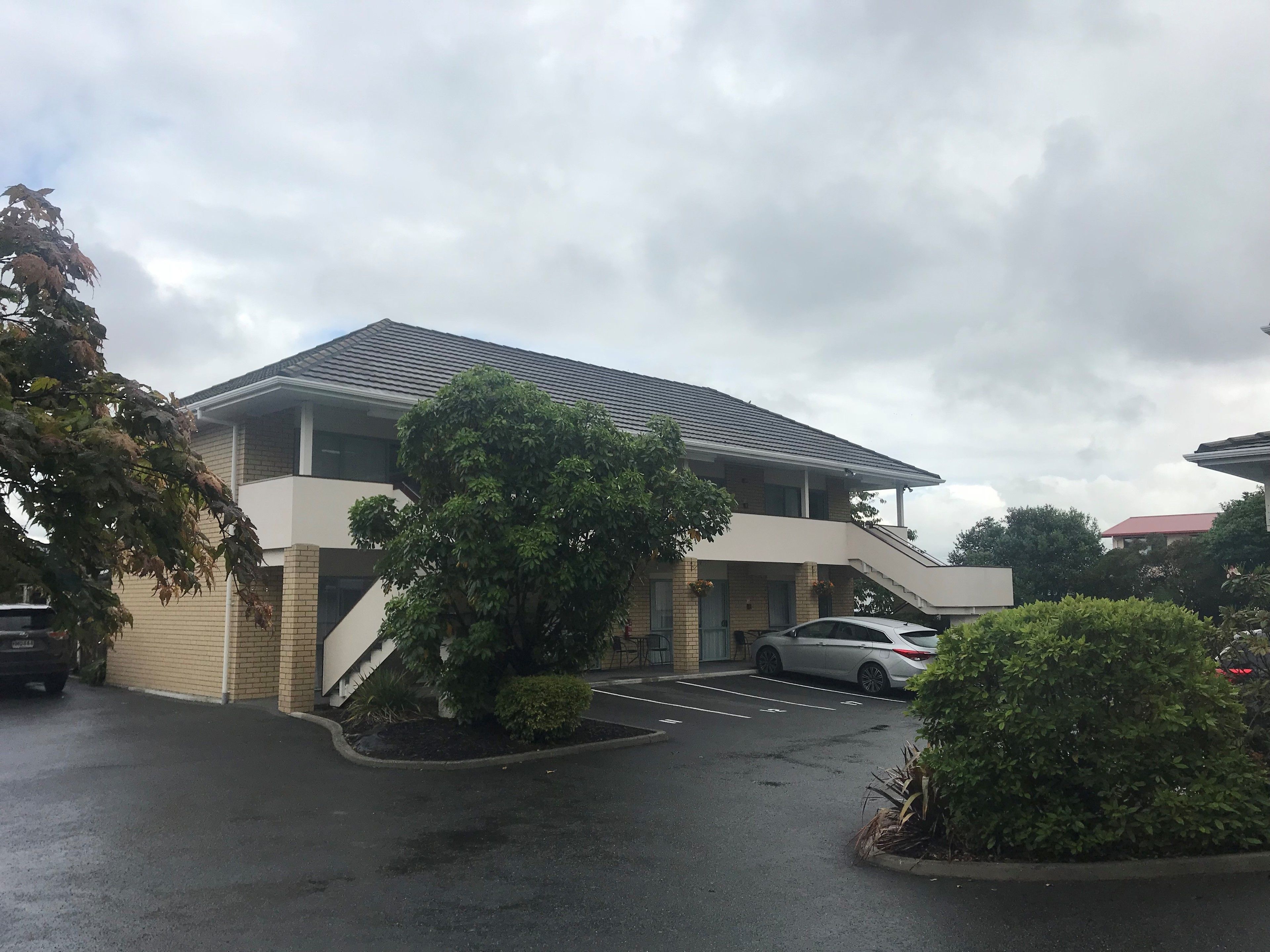 A two-story building with a flat roof and a parking area in front.