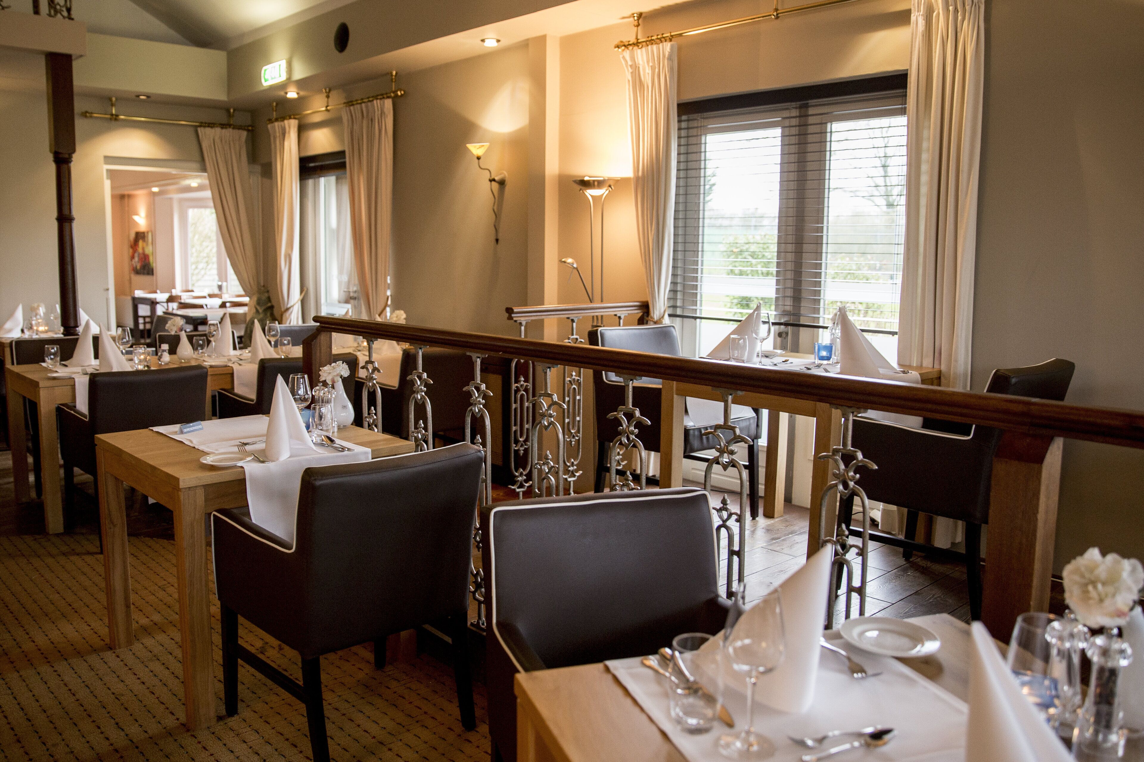 A dining area with tables set for service, chairs, and a view of the outdoors through large windows.