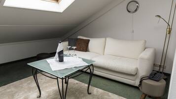 Una habitación con una mesa de vidrio, un sofá blanco, un espejo redondo pequeño y una lámpara de pie.