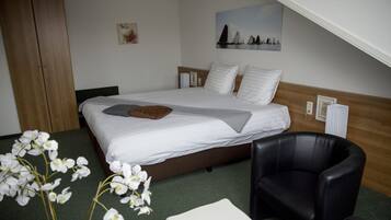 Camera d'albergo con un letto, una poltrona in pelle nera, un tavolino e orchidee bianche sul pavimento.