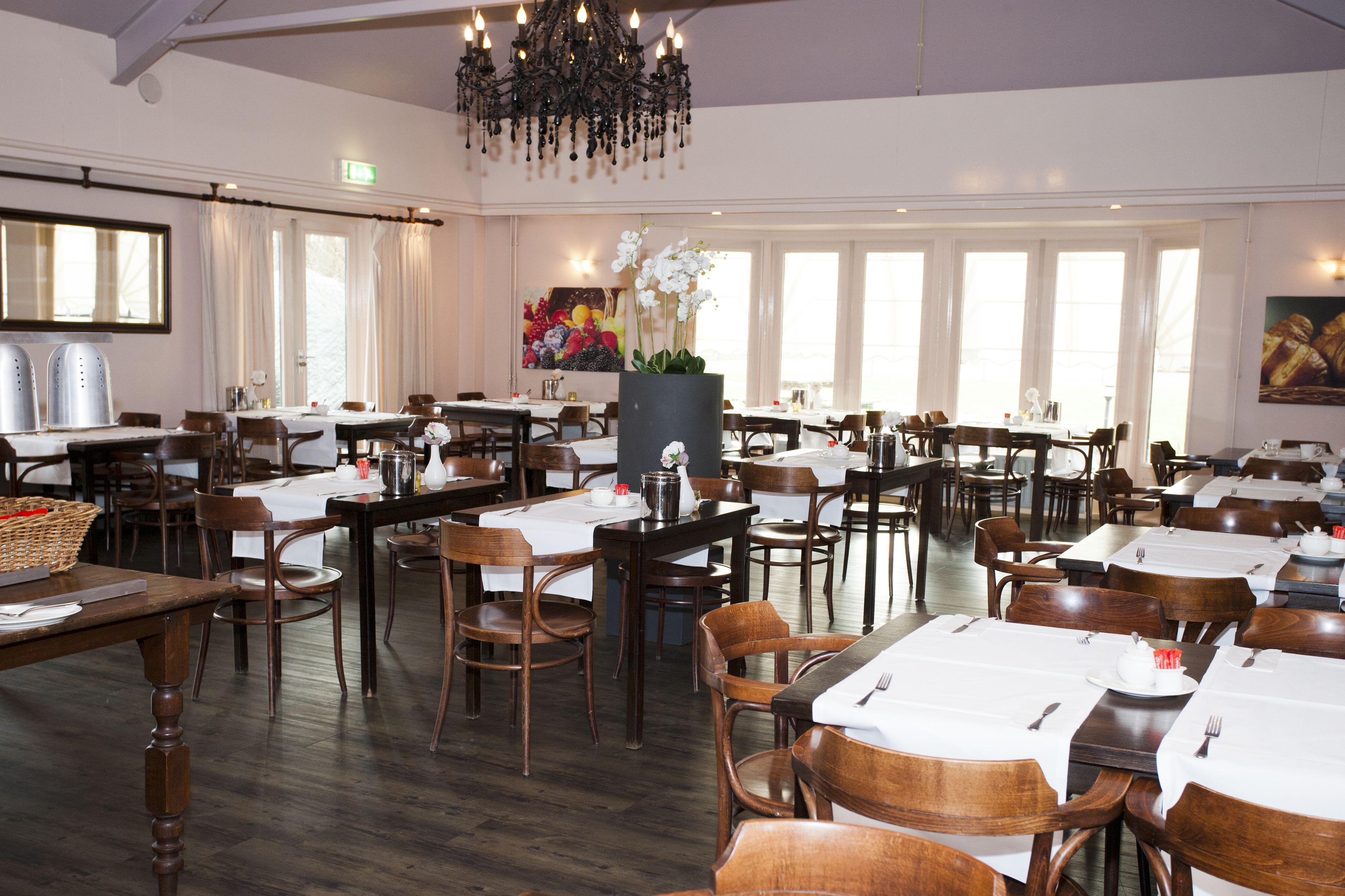 A spacious dining area with multiple tables and chairs, a chandelier, and large windows allowing natural light.
