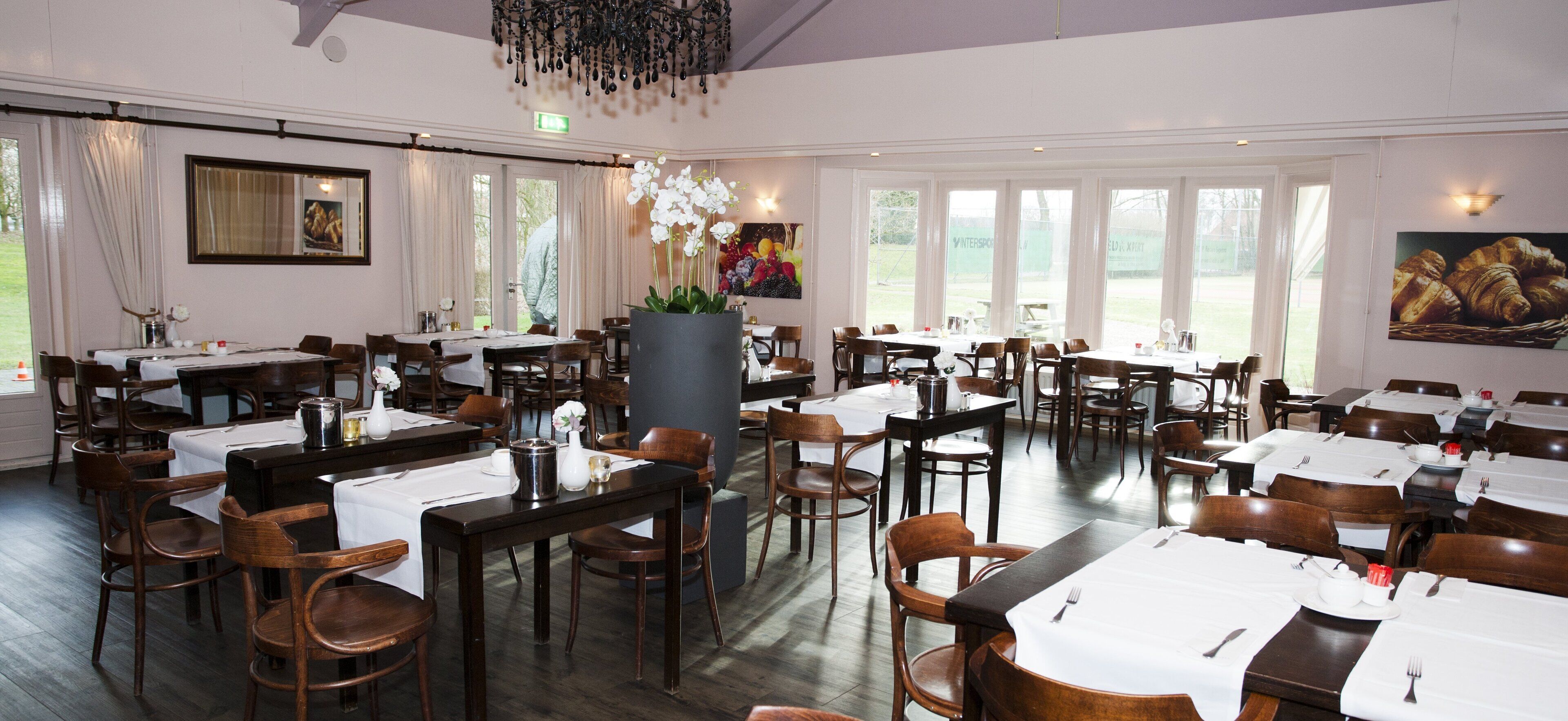 Ein Restaurant mit mehreren Tischen, Stühlen, großen Fenstern und einer Kristallleuchter.