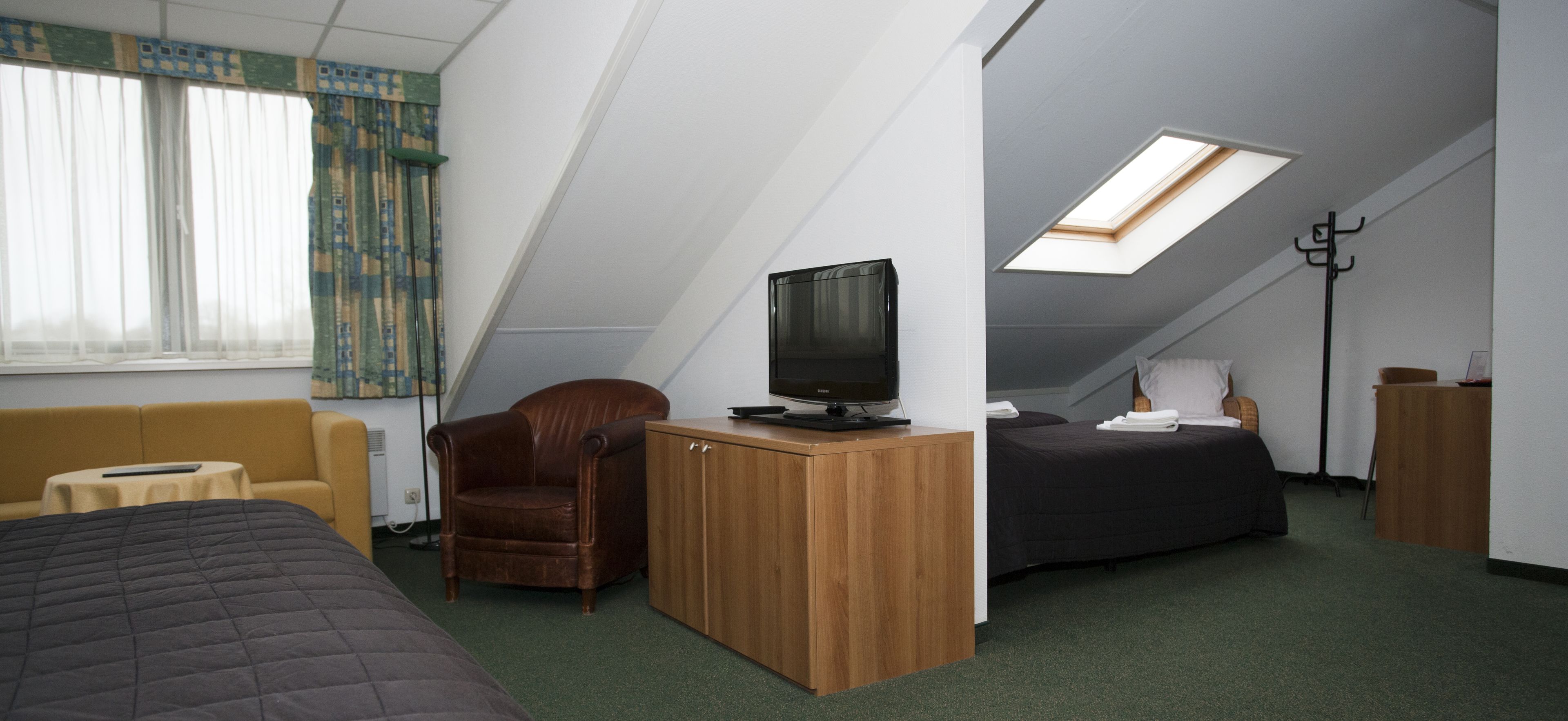 Habitación compacta con una cama, un escritorio con televisor, una silla y una cama con cubierta oscura.
