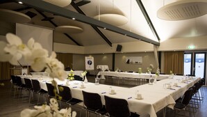 Un salón de conferencias con largas mesas, sillas y un escenario.