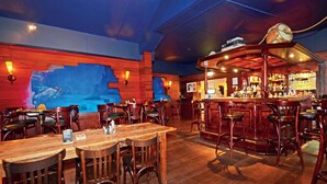 Un restaurante con mesas y sillas de madera, una zona de bar y un mural en la pared.