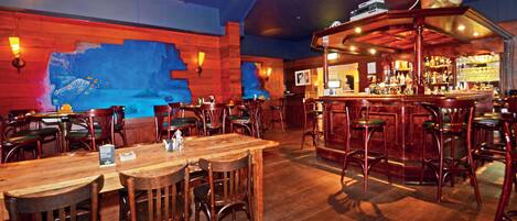 A restaurant with wooden tables and chairs, a bar area, and a mural on the wall.