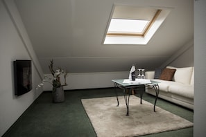 Ein modernes Schlafzimmer im Loft-Stil mit Dachfenster, einem Glastisch, einem weißen Sofa und einer Topfpflanze.